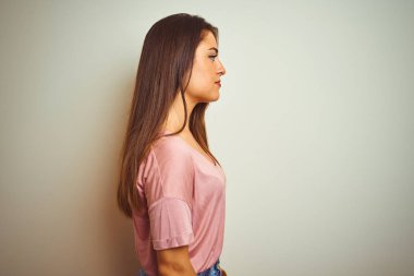 Yan bakarak izole beyaz arka plan üzerinde duran rahat t-shirt giyen genç güzel kadın, kendine güvenen gülümseme ile doğal yüz ile profil poz dinlenmek.