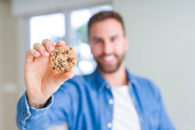 Yakışıklı adam mutlu bir yüz ayakta ve dişleri gösteren kendinden emin bir gülümseme ile gülümseyerek çikolata cips çerezleri yeme