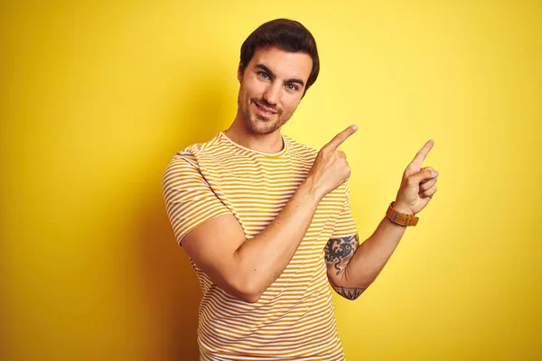 노란색 줄무늬 티셔츠를 문신을 남자는 미소를 지으며 손가락으로 가리키는 카메라를 — 스톡 사진