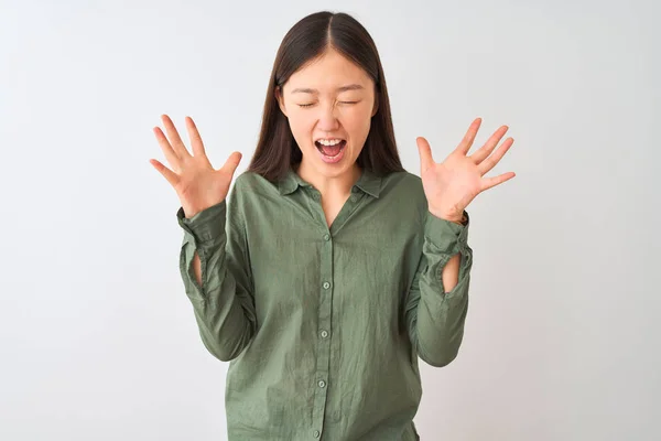 年轻的中国妇女穿着休闲的绿色衬衫站在孤立的白色背景庆祝疯狂和疯狂的成功与手臂抬起和闭上眼睛尖叫兴奋 优胜者概念 — 图库照片
