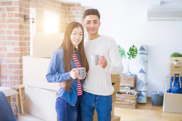 Beautiful young asian couple with coffee cups looking happy and smiling excited moving to a new home