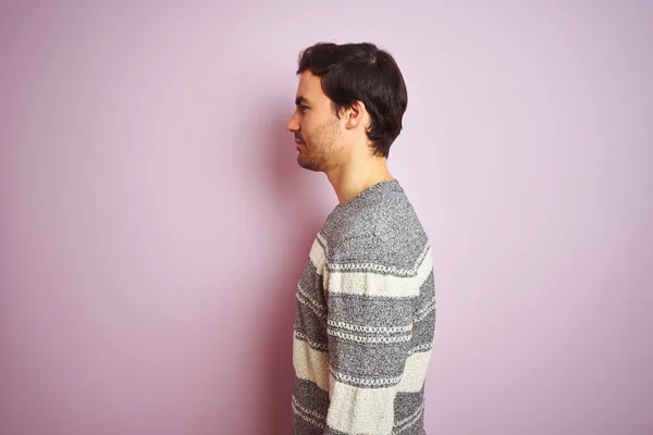 カジュアルなストライプのセーターを着た若いハンサムな男性が横を向いて孤立したピンクの背景の上に立って 自信のある笑顔で自然な顔でプロフィールポーズをリラックス — ストック写真