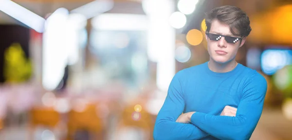 Young man wearing funny thug life glasses over isolated background skeptic and nervous, disapproving expression on face with crossed arms. Negative person.