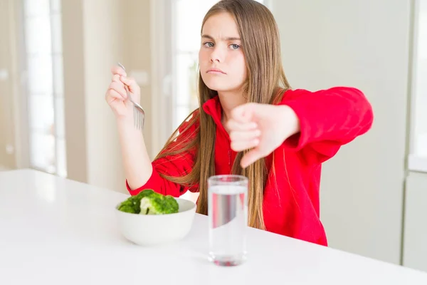 新鮮なブロッコリーを食べ 怒った顔で水を飲む美しい若い女の子 親指を下に嫌いを示す否定的なサイン 拒絶概念 — ストック写真