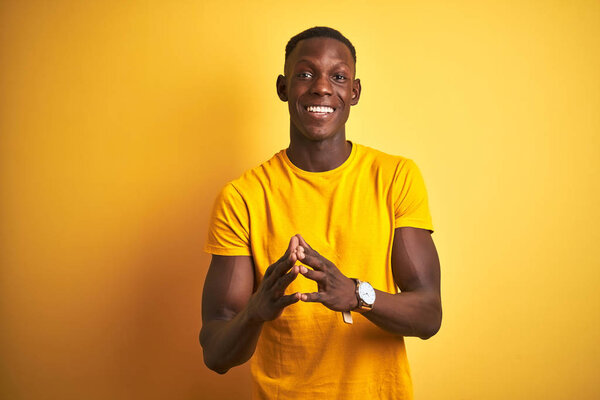 Young african american man wearing casual t-shirt standing over isolated yellow background Hands together and fingers crossed smiling relaxed and cheerful. Success and optimistic