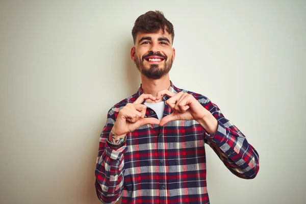 Young man wearing casual shirt standing over isolated white background smiling in love showing heart symbol and shape with hands. Romantic concept.