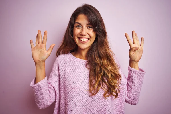ピンクの孤立した背景の上に立つセーターを着た若い美しい女性は 自信を持って幸せに微笑みながら 指番号9を示し 指を指差し — ストック写真