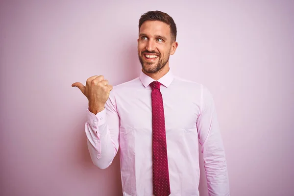 穿着领带和优雅的衬衫在粉红色孤立的背景商务男子微笑着与快乐的脸看 并指着一边竖起大拇指 — 图库照片