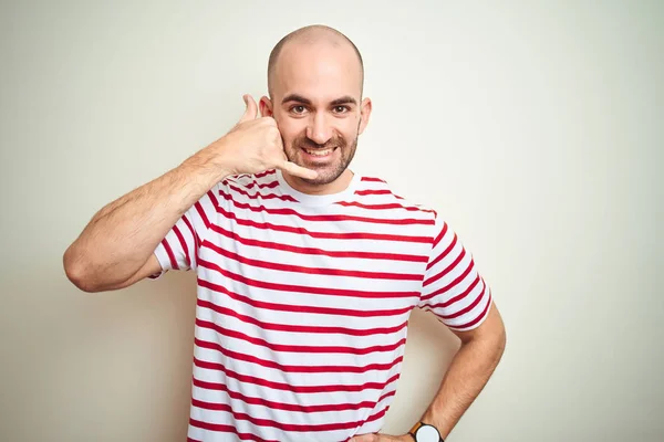 Young bald man with beard wearing casual striped red t-shirt over white isolated background smiling doing phone gesture with hand and fingers like talking on the telephone. Communicating concepts.
