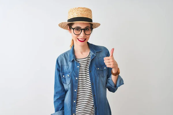 Redhead woman wearing denim shirt glasses and hat over isolated white background doing happy thumbs up gesture with hand. Approving expression looking at the camera with showing success.