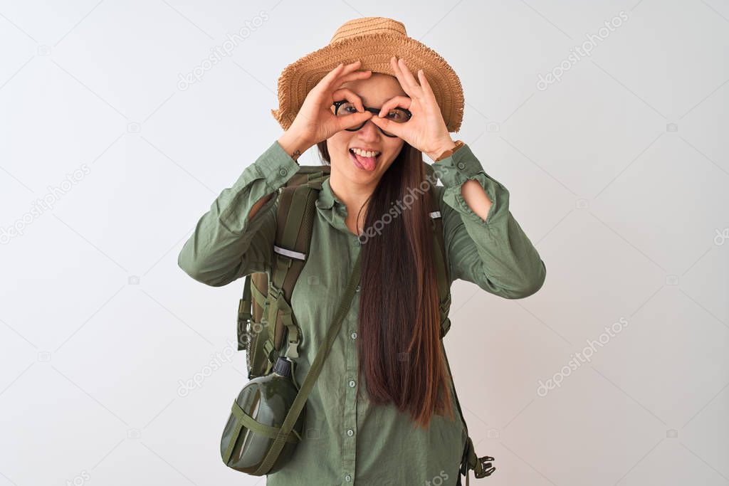 Chinese hiker woman wearing canteen hat glasses backpack over isolated white background doing ok gesture like binoculars sticking tongue out, eyes looking through fingers. Crazy expression.