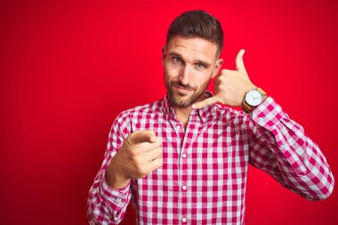 Kırmızı izole arka plan üzerinde genç yakışıklı adam telefon jest konuşurken ve size işaret ediyor. Beni ara.