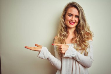 Beyaz izole arka plan üzerinde ayakta genç güzel kadın hayran ve el ile sunmak ve parmak ile işaret ederken kameraya gülümsüyor.