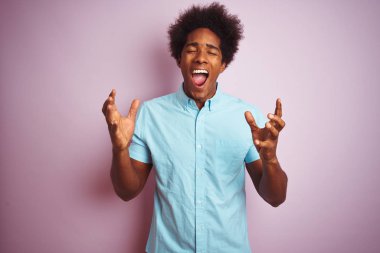 Afro saç ile genç Amerikalı adam mavi gömlek ayakta izole pembe arka plan üzerinde duran deli ve silah ile başarı için çılgın kutluyor ve kapalı gözleri heyecanlı çığlık kaldırdı. Kazanan kavramı