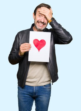 Kırmızı kalp ile kağıt tutan yakışıklı orta yaş adam baş el ile vurguladı, utanç ve sürpriz yüz ile şok, öfkeli ve sinirli. Korku ve hata için üzgün.