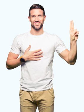Rahat beyaz t-shirt giyen yakışıklı adam göğsüne ve parmaklara el ile küfür, sadakat vaat yemini yapma