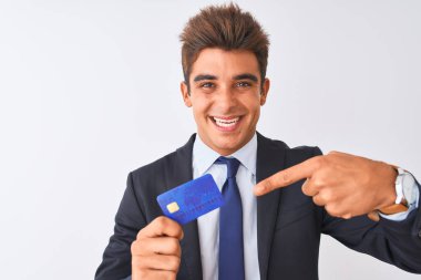 Genç yakışıklı işadamı takım elbise giyen izole beyaz arka plan üzerinde kredi kartı tutan çok mutlu el ve parmak ile işaret