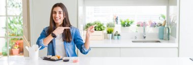 Güzel genç kadının geniş açı resim yemek teslimat suşi gülümseyen ve kamera iki el ve parmak tarafına işaret bakarak.