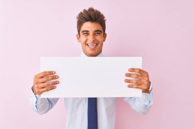 Genç yakışıklı işadamı mutlu bir yüz ayakta ve dişleri gösteren kendinden emin bir gülümseme ile gülümseyerek izole pembe arka plan üzerinde duran afiş tutan