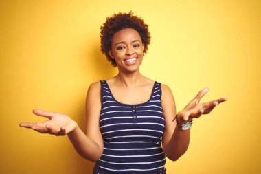 Sevimli Afrikalı Amerikan kadın arka plan üzerinde izole sarı el gömlek giyen yaz yardım vermek ve kabul neşeli sunar.