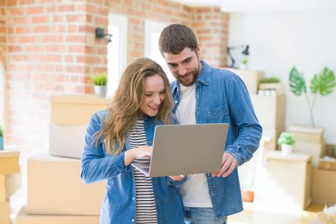 Yeni bir daireye taşımak için mutlu karton kutular etrafında bir odada bilgisayar laptop ayakta kullanarak genç çift