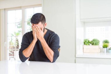 Yakışıklı İspanyol adam ağlarken elleri ile yüz kapsayan üzücü ifade ile evde rahat kazak giyiyor. Depresyon konsepti.