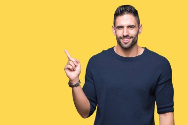 Yüz üzerinde büyük bir gülümseme ile izole arka plan üzerinde kazak giyen genç yakışıklı adam, kamera bakarak yan el ve parmak ile işaret.