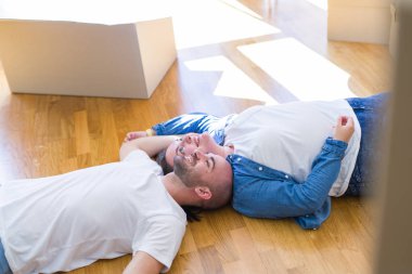 Yeni bir evin katında yatan aşık genç çift, yeni bir daireye taşınmak için çok mutlu gülümseyen, karton kutular civarı