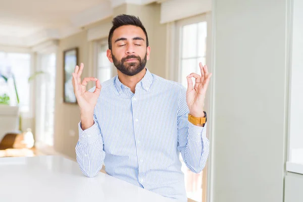 Handsome hispanic business man relax and smiling with eyes closed doing meditation gesture with fingers. Yoga concept.