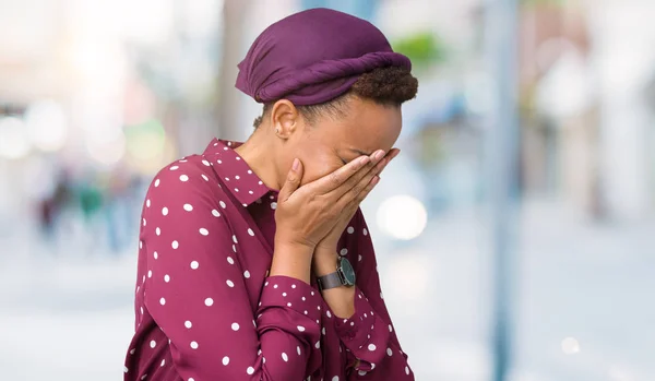 Beautiful young african american woman wearing head scarf over isolated background with sad expression covering face with hands while crying. Depression concept.