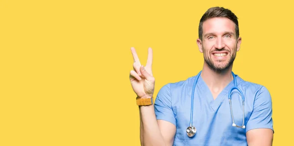 帅气的医生穿着医疗制服在孤立的背景上微笑着 高兴的脸对着镜头眨眼做胜利的标志 — 图库照片