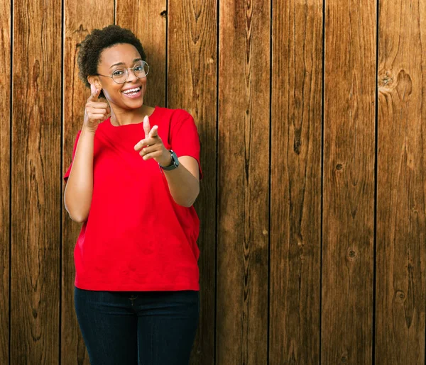 Fotoğraf makinesi ile mutlu ve komik yüz için parmakları işaret izole arka plan üzerinde gözlük güzel genç Afro-Amerikan kadın. İyi enerji ve vibes.