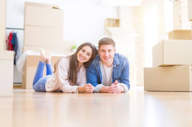 Evde karton kutular etrafında yerde yatan rahatlatıcı genç güzel çift, yeni bir eve hareket mutlu gülümseyen