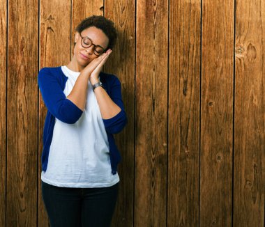 Uyku yorgun hayal ve ellerle birlikte poz ile kapalı gözler gülümseyen izole arka plan üzerinde gözlük takan genç güzel Afrikalı-Amerikalı kadın.