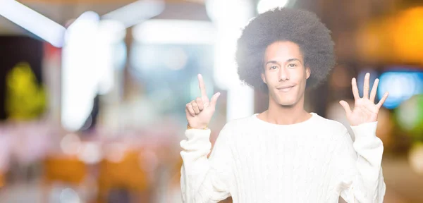 アフロ髪着て冬セーターを示すと指で上向きに若いアフリカ系アメリカ人の数は自信を持って 幸せな笑みを浮かべている間 — ストック写真