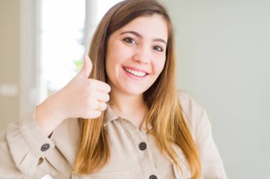 Güzel genç kadın evde mutlu Yaşasın el hareketini yapıyor. Kameraya bakarak başarı gösteren ile ifade onaylama.