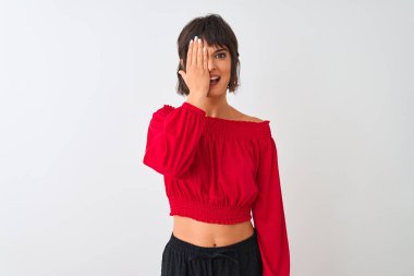 Kırmızı yazlık t-shirt giyen genç güzel kadın el ile bir göz kapsayan izole beyaz arka plan üzerinde duran, yüzünde kendine güvenen gülümseme ve sürpriz duygu.