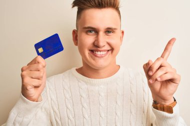 Genç yakışıklı adam izole beyaz arka plan üzerinde kredi kartı tutan çok mutlu yan el ve parmak ile işaret