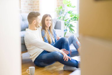 Yeni bir daire zemin üzerinde oturan genç güzel çift, yeni bir eve taşınmak için mutlu sevgi gülümsüyor