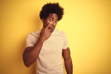 Afro saçlı Amerikan adam izole sarı arka plan üzerinde ayakta çizgili t-shirt giyen seni jest izlerken göz Işaret, şüpheli ifade