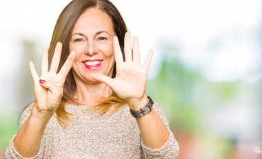 Güzel orta yaş kadın gösteren moda kazak giyen ve parmak sayısı dokuz ile işaret ederken emin ve mutlu gülümseyen.