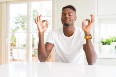 Evde beyaz masada yakışıklı Afrikalı Amerikalı adam rahatlayın ve gözleri ile gülümseyen meditasyon jest parmaklar ile kapalı. Yoga konsepti.