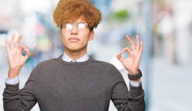 Afro saç gözlük giyen genç yakışıklı iş adamı rahatlayın ve gözleri ile gülümseyen meditasyon jest parmaklar ile kapalı. Yoga konsepti.