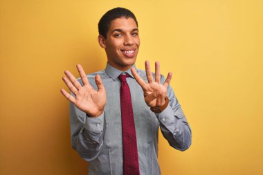 Genç yakışıklı Arap işadamı gömlek giyen ve izole sarı arka plan üzerinde kravat gösteren ve parmakları ile işaret ederken emin ve mutlu gülümseyerek dokuz.