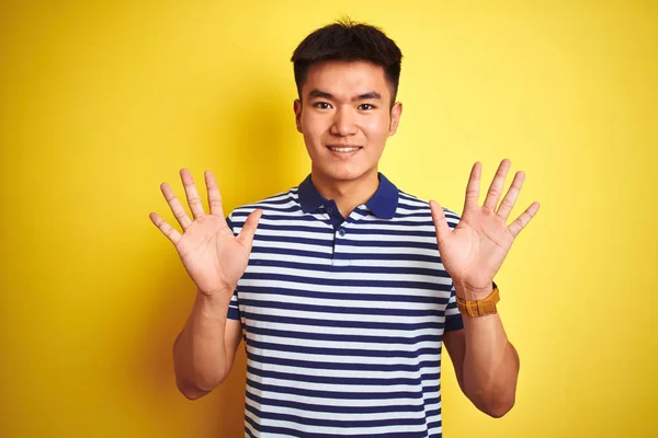 孤立した黄色の背景の上に立つストライプのポロを着た若いアジアの中国人男性は 自信を持って幸せに微笑みながら 指番号10を示し 指を上げる — ストック写真