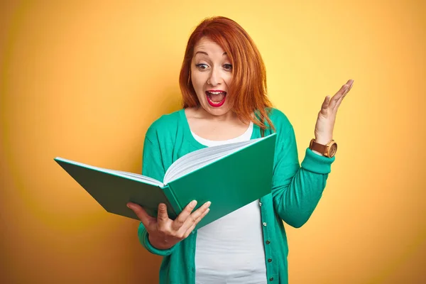 Young Redhead Student Woman Reading Green Book Yellow Isolated Background — Stock Photo, Image