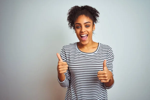 African american woman wearing navy striped t-shirt standing over isolated white background success sign doing positive gesture with hand, thumbs up smiling and happy. Cheerful expression and winner gesture.