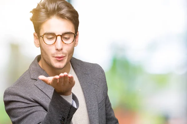 Young business man wearing glasses over isolated background looking at the camera blowing a kiss with hand on air being lovely and sexy. Love expression.