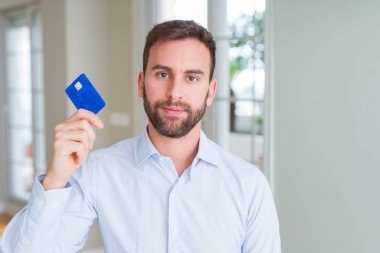 Handsome business man holding credit card with a confident expression on smart face thinking serious clipart