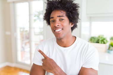 Beyaz t-shirt giyen Afro-Amerikan adam yüzünde mutlu ve doğal ifade ile yan yana el ve parmak işaret yüz bir gülümseme ile neşeli